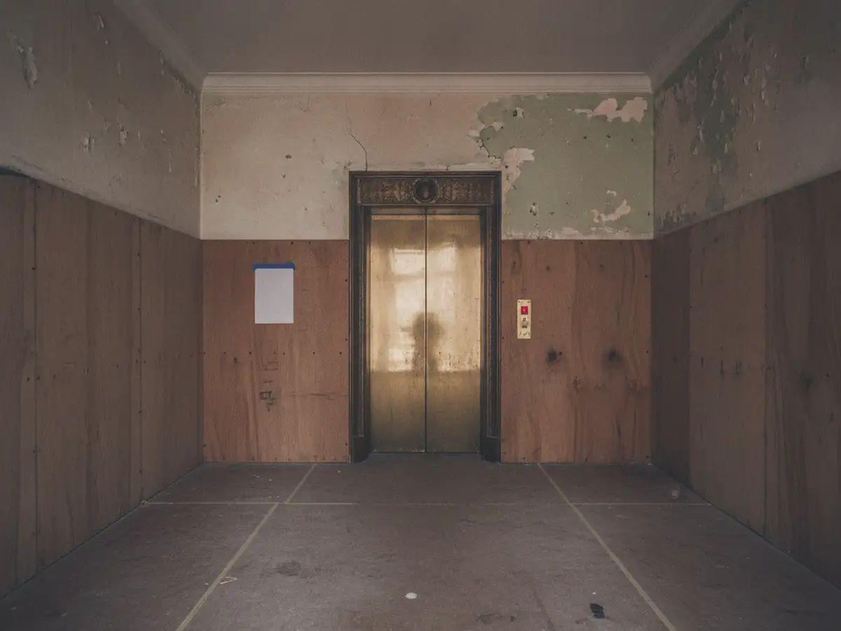 The lobby of a pre-war Bronx apartment building with its single elevator door, the terrazzo floor and walls covered in protective board.